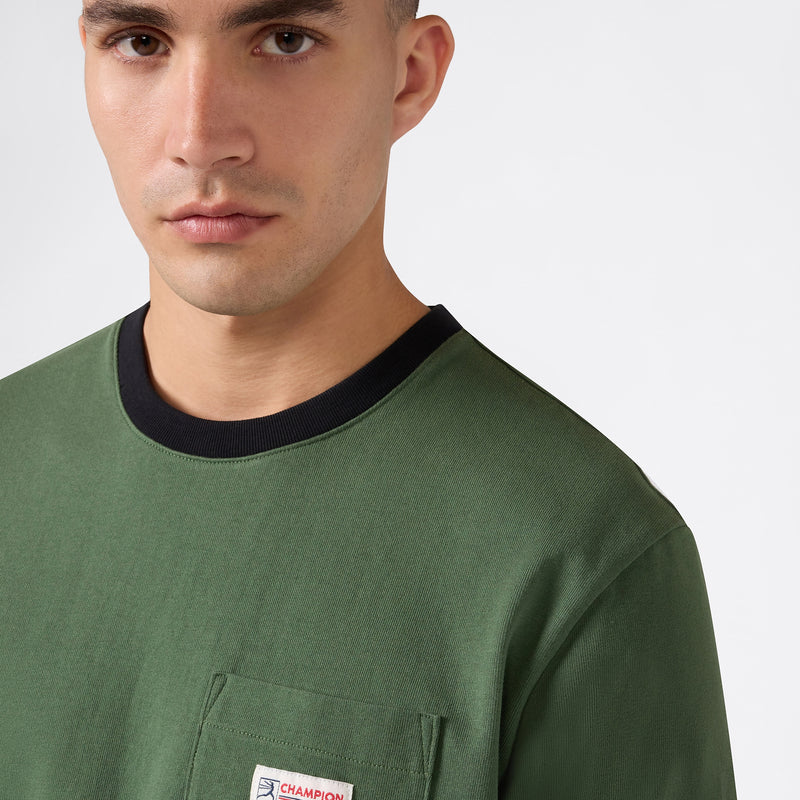 A person wearing the Champion Men’s Knitted Ringer T-Shirt in green, featuring a black collar and a small left-side pocket, made from soft cotton jersey, stands against a plain white background.