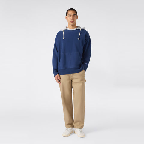 A person stands facing forward, wearing a Champion Men’s Knitted Hooded Sweatshirt (Vintage Wash) with white drawstrings, paired with khaki pants and white sneakers against a plain light background.