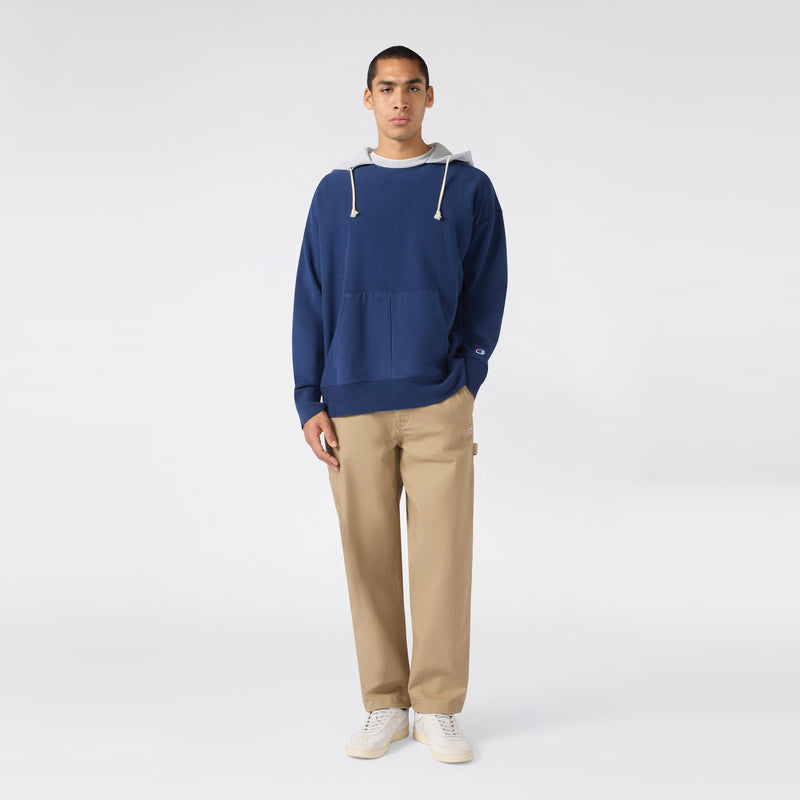 A person stands facing forward, wearing a Champion Men’s Knitted Hooded Sweatshirt (Vintage Wash) with white drawstrings, paired with khaki pants and white sneakers against a plain light background.