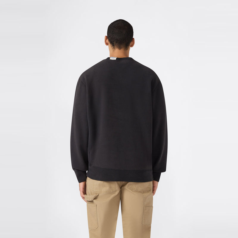 A person stands facing away, wearing a black Champion Men’s Knitted Crewneck Sweatshirt featuring a vintage wash and reversible design, paired with beige cargo pants against a plain white background.