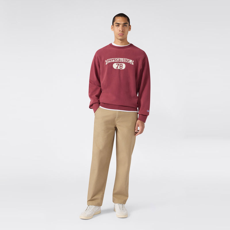 A person stands against a plain background, wearing a maroon Champion Men’s Knitted Crewneck Sweatshirt (Reversible + Vintage Wash), paired with beige pants and white sneakers.