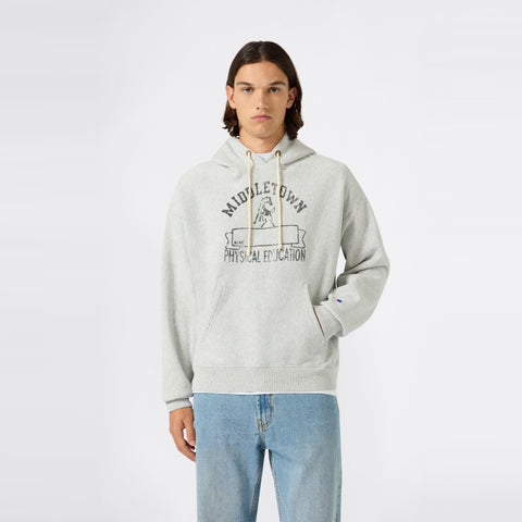 A young person with long brown hair wears a light gray Champion Men’s Knitted Hooded Sweatshirt, paired with light blue jeans and standing against a plain white background.