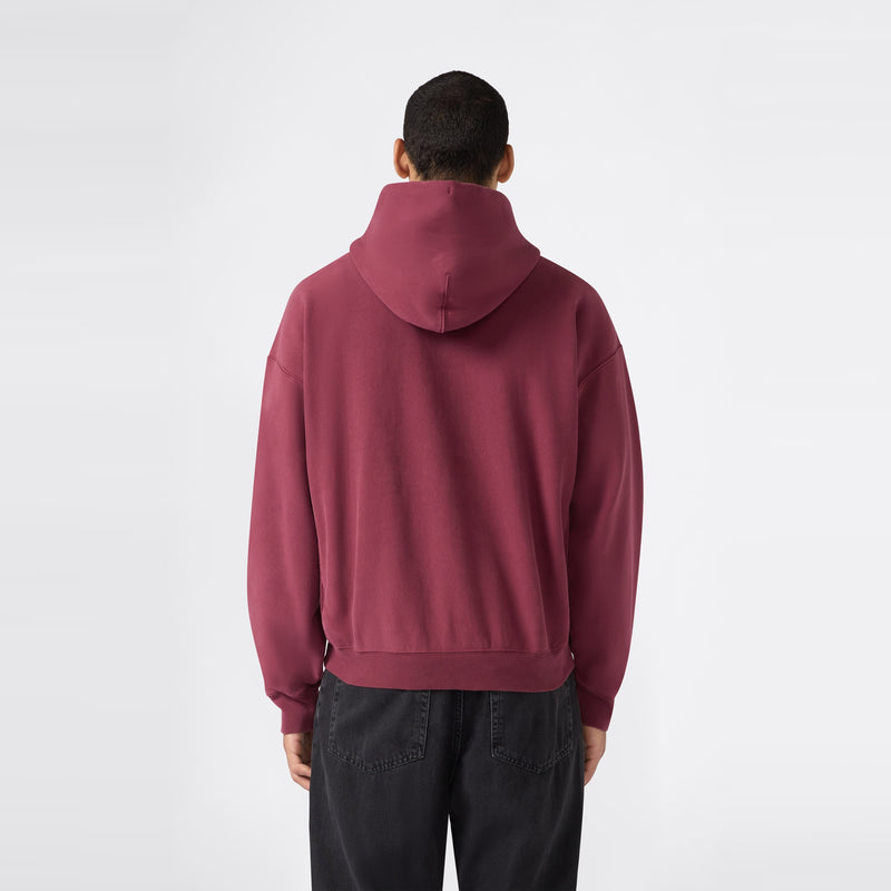 A person wearing a maroon Men’s Knitted Hooded Sweatshirt by Champion and black jeans stands facing away from the camera against a plain white background.