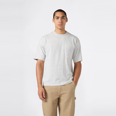 A man stands against a plain white background, wearing the Champion Men’s Knitted T-Shape Tee paired with khaki pants, one hand in his pocket and a neutral expression—perfectly embodying the effortless style of modern men’s sportswear.