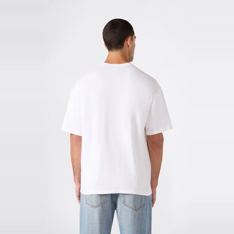 A man stands with his back to the camera, wearing the Champion Men’s Knitted T-Shape Tee paired with light blue jeans, set against a minimalist light gray background.
