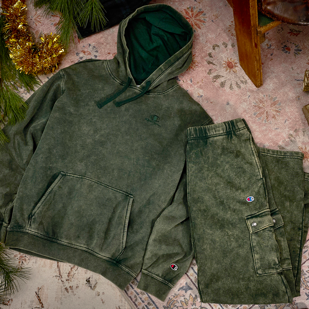 Green hoodie and pants laid out on a patterned rug with Christmas decorations.