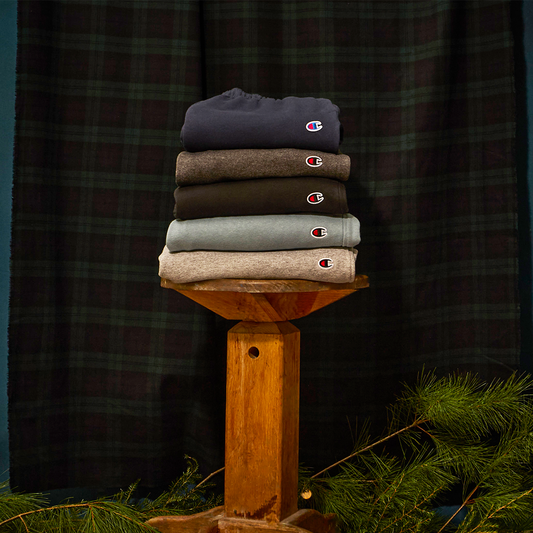Stack of folded Champion shirts on a wooden stand with a dark plaid background