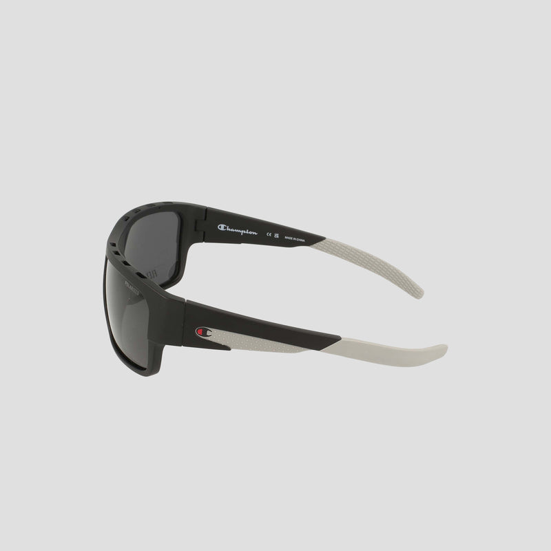 Champion Men's Polarized Grilamid Flex Grip Tip - Large sunglasses feature black frames with dark lenses, complemented by gray textured arms and a small red-and-white Champion logo near the hinges. Engineered for ultra-lightweight comfort, these sunglasses are ideal for prolonged wear. Set against a light gray background, the product is displayed from a side and slightly rear angle.