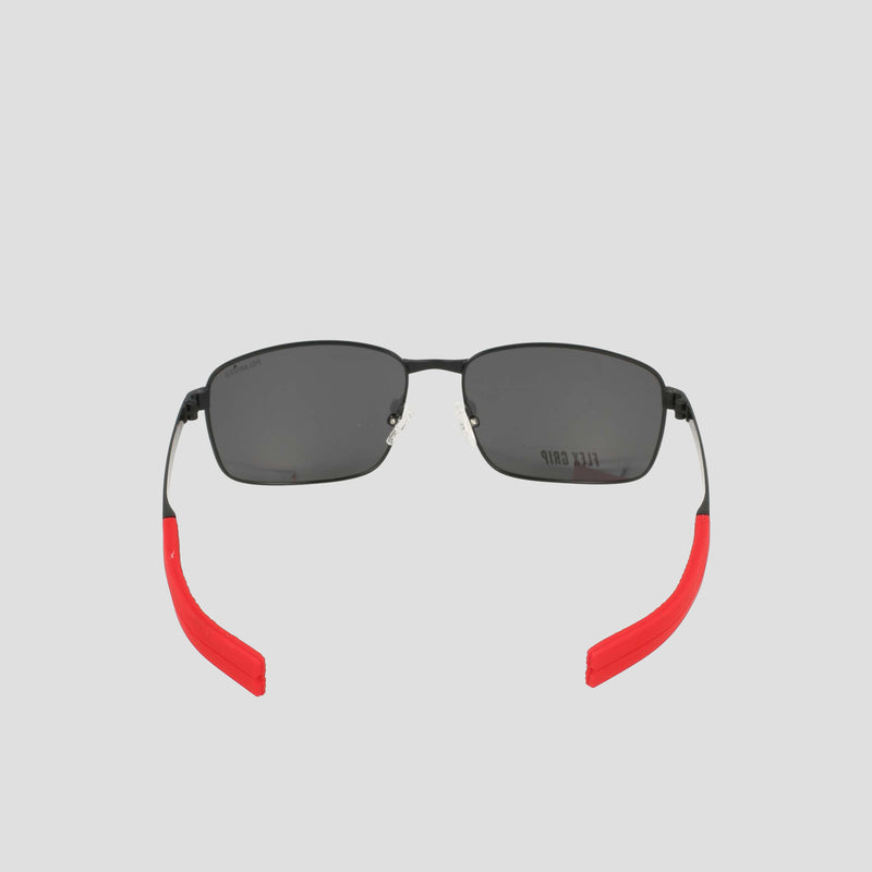 Champion Men’s Polarized Stainless ST-Shirtl Flex Grip Tip sunglasses with a black rectangular frame and polarized lenses, accented by bright red flex grip ear tips, are showcased on a plain light gray background. Designed for active lifestyles with a retainer-inspired frame, the sunglasses are positioned facing forward with slightly open arms.