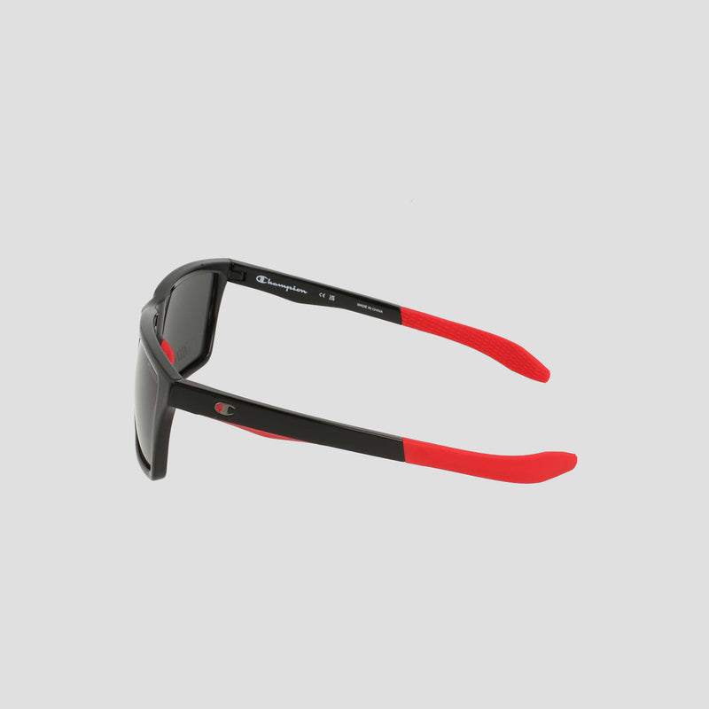 Men's Polarized Grilamid Flex Grip Tip - Medium sunglasses by Champion shown from a side angle on a light gray background. These sunglasses feature a black frame with red arms, and the inside of the left arm displays the Champion logo and size details in white text. Crafted from lightweight TR90 material, they are designed for comfort and durability.