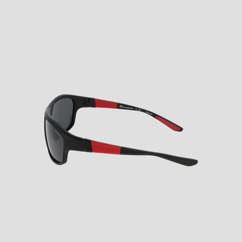 Men’s Polarized Comfort Fit - Large by Champion, black sunglasses with red accents on the arms, shown from a side angle. Featuring a durable TR90 frame and adjustable rubber tips for enhanced comfort, the arms are marked with a white Champion logo. The polarized dark lenses are set against a light gray background.