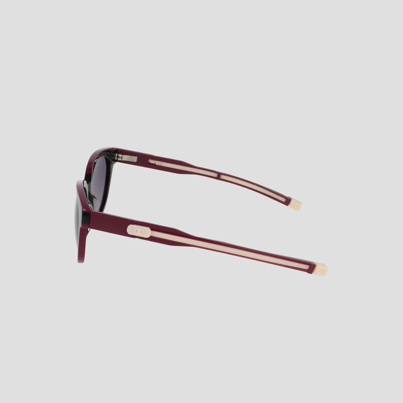 Side view of Champion Women's Polarized Retainer Round sunglasses in maroon with beige temple accents, featuring dark polarized lenses and a minimalist modern design, set against a plain light gray background.