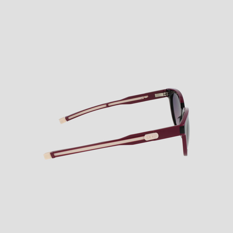 Side view of Champion Women's Polarized Retainer Round sunglasses, featuring dark polarized lenses, burgundy frames, and light tan arm accents, displayed against a plain light gray background.