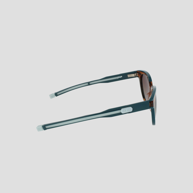 Side view of Champion Women's Polarized Retainer Round eyewear in teal with brown-tinted lenses and silver arm accents, displayed against a plain white background.