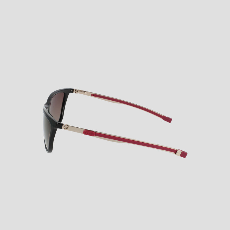 The Champion Women's Polarized Retainer Rectangle sunglasses feature a black rectangle frame with gold accents and red arms, highlighted by a subtle logo detail near the hinge. Shown from the side against a light gray background, these athleisure eyewear pieces blend style with performance thanks to their dark polarized lenses.