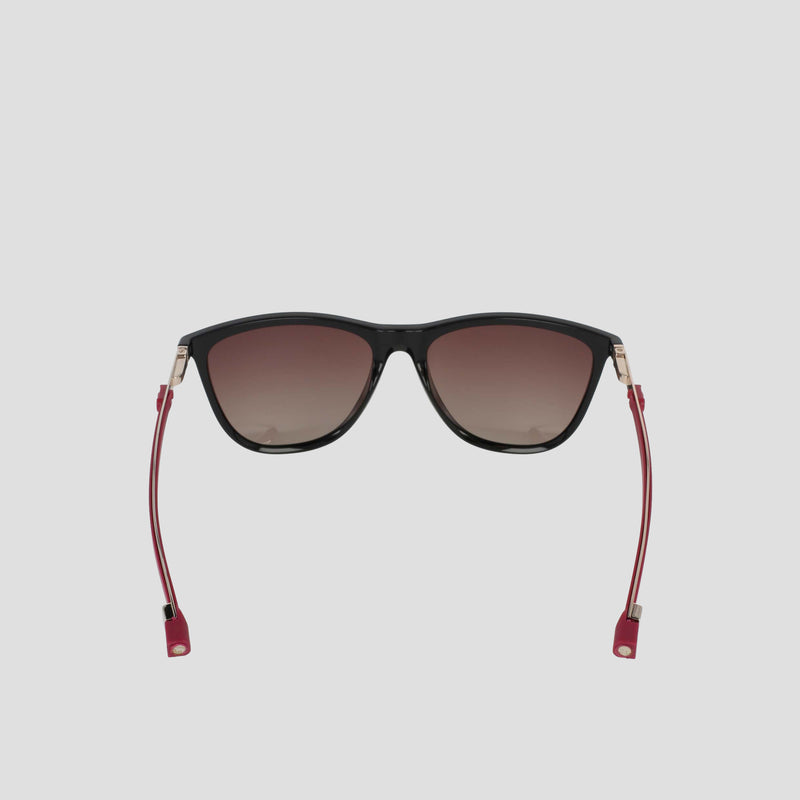 Front-facing view of the Champion Women's Polarized Retainer Rectangle sunglasses, featuring a black cateye design with dark gradient polarized lenses, thin red temples, and gold accents—ideal athleisure eyewear—displayed against a plain light gray background.