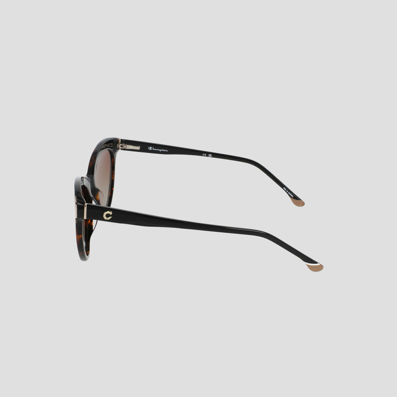 Side view of the Champion Women's Polarized Cateye sunglasses featuring a tortoiseshell design, black arms, gold accents, and brown-tinted lenses, displayed on a plain light gray background. The RX-able frame offers versatility for prescription wearers.