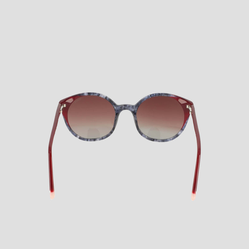The Champion Women's Polarized Flirty Round sunglasses are displayed against a plain light gray background, featuring marbled gray handmade acetate frames, red gradient lenses, and coordinating red arms. These unique shades blend retro-inspired accents with modern sophistication.