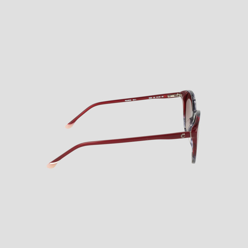 Side view of Champion Women's Polarized Flirty Round sunglasses, featuring red cat-eye frames handmade from translucent acetate with light-colored temple tips, displayed on a plain light gray background.