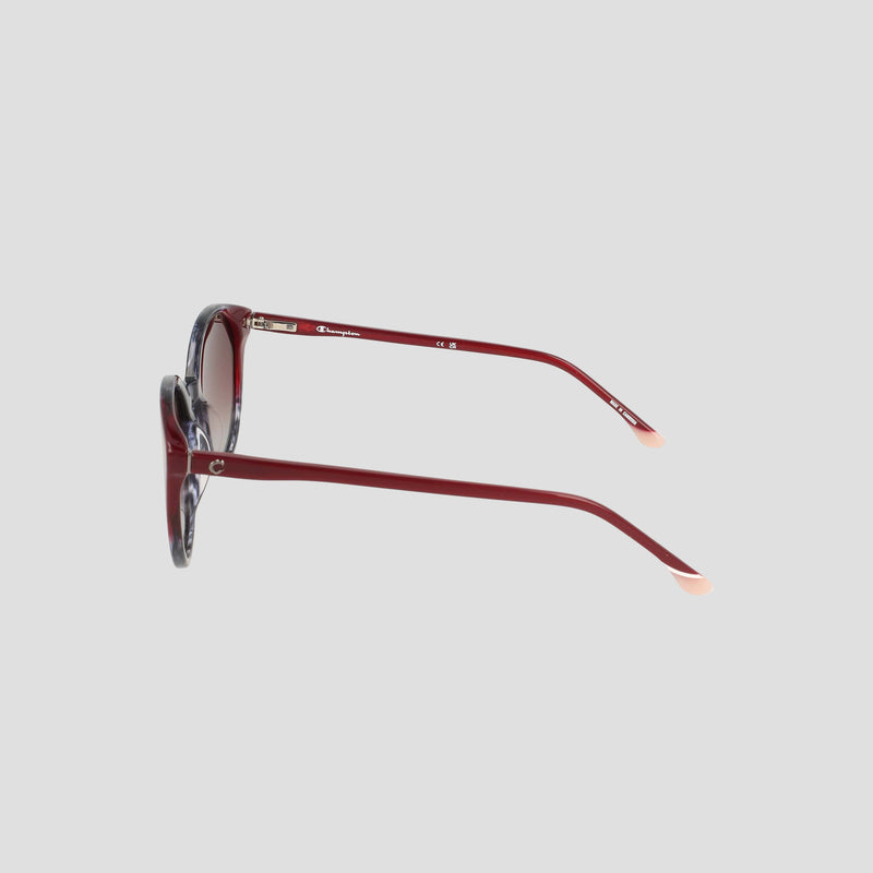 Side view of the Champion Women's Polarized Flirty Round eyeglasses featuring red, round frames crafted from handmade acetate and light-colored tips on the arms, set against a plain light gray background.