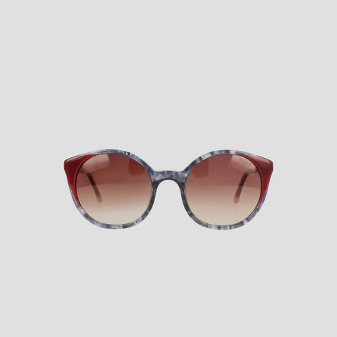 The Champion Women's Polarized Flirty Round sunglasses feature gradient brown polarized lenses, marbled gray handmade acetate frames, and solid dark red accents on the upper corners, shown against a plain light gray background.