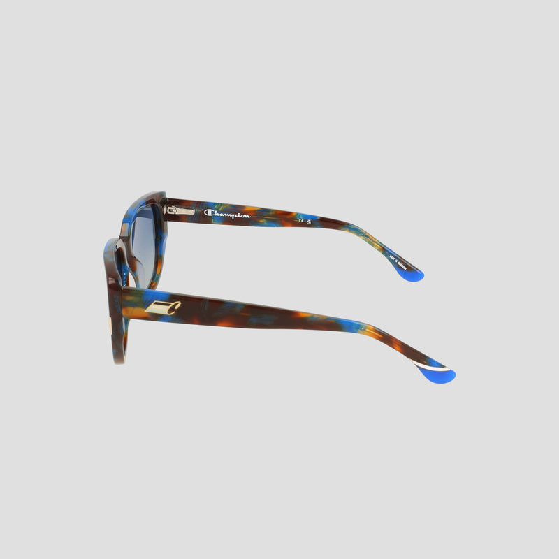 Side view of the Champion Women's Polarized Modified Cateye sunglasses, featuring a tortoiseshell frame with blue-tipped arms, expertly crafted from handmade acetate for a touch of luxury. Small printed logos and text appear on the inside of the left arm. Set against a light gray background.