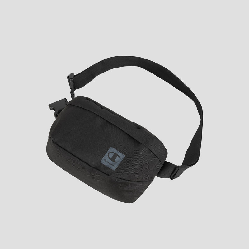 A black Champion Atlas Waist Pack with an adjustable strap and buckle, showcasing a small square patch with the iconic Champion logo on the front, photographed against a light gray background. This athletic bag provides adventure-ready storage for your essentials wherever you go.