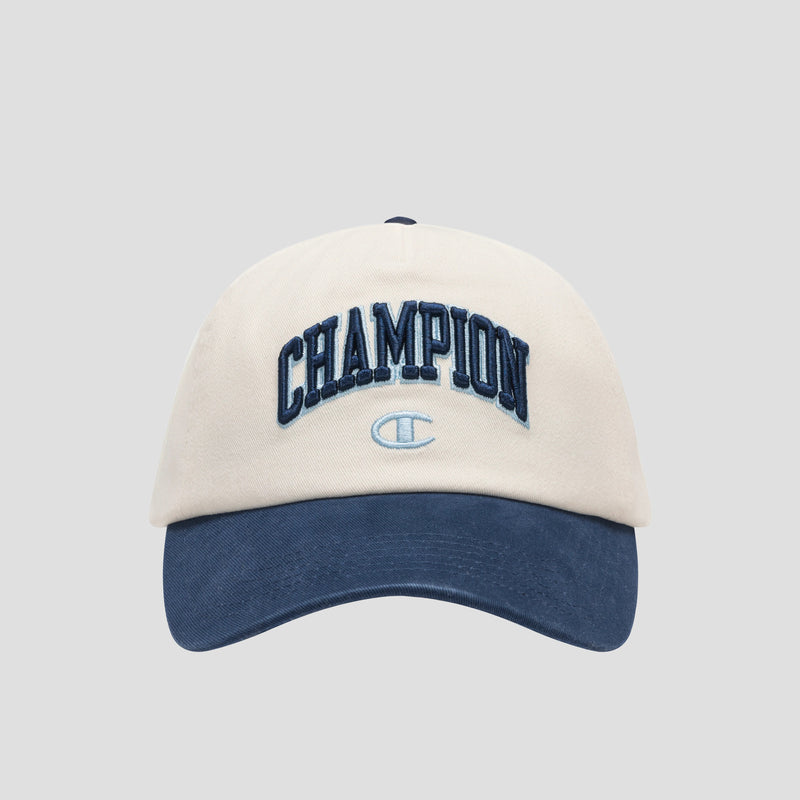 A beige and navy blue Amor Adjustable Baseball Cap by Champion, crafted from washed cotton twill and featuring “CHAMPION” embroidered in dark blue lettering on the front with a small Champion logo below, photographed on a plain gray background—showcasing true Champion authenticity.
