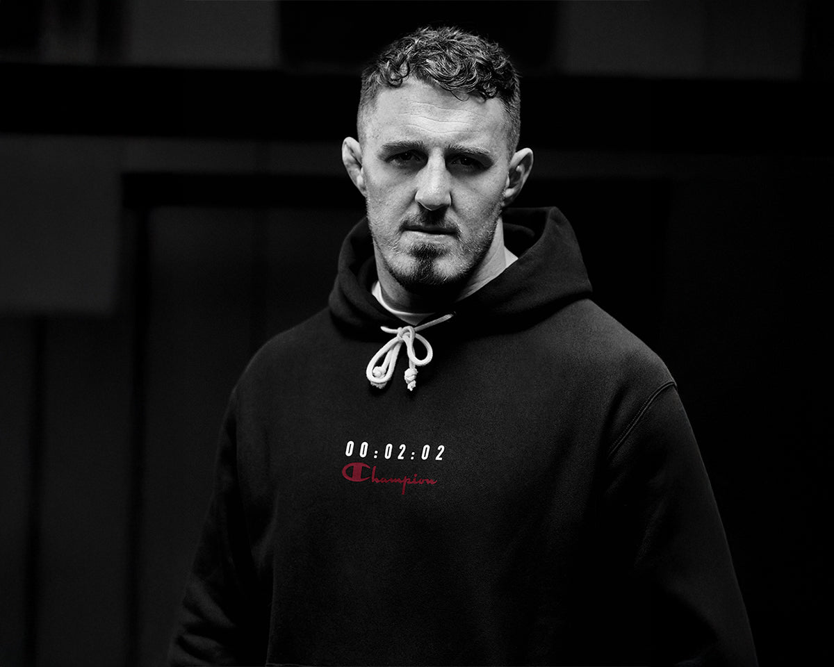 Man wearing a black hoodie with a logo on a dark background