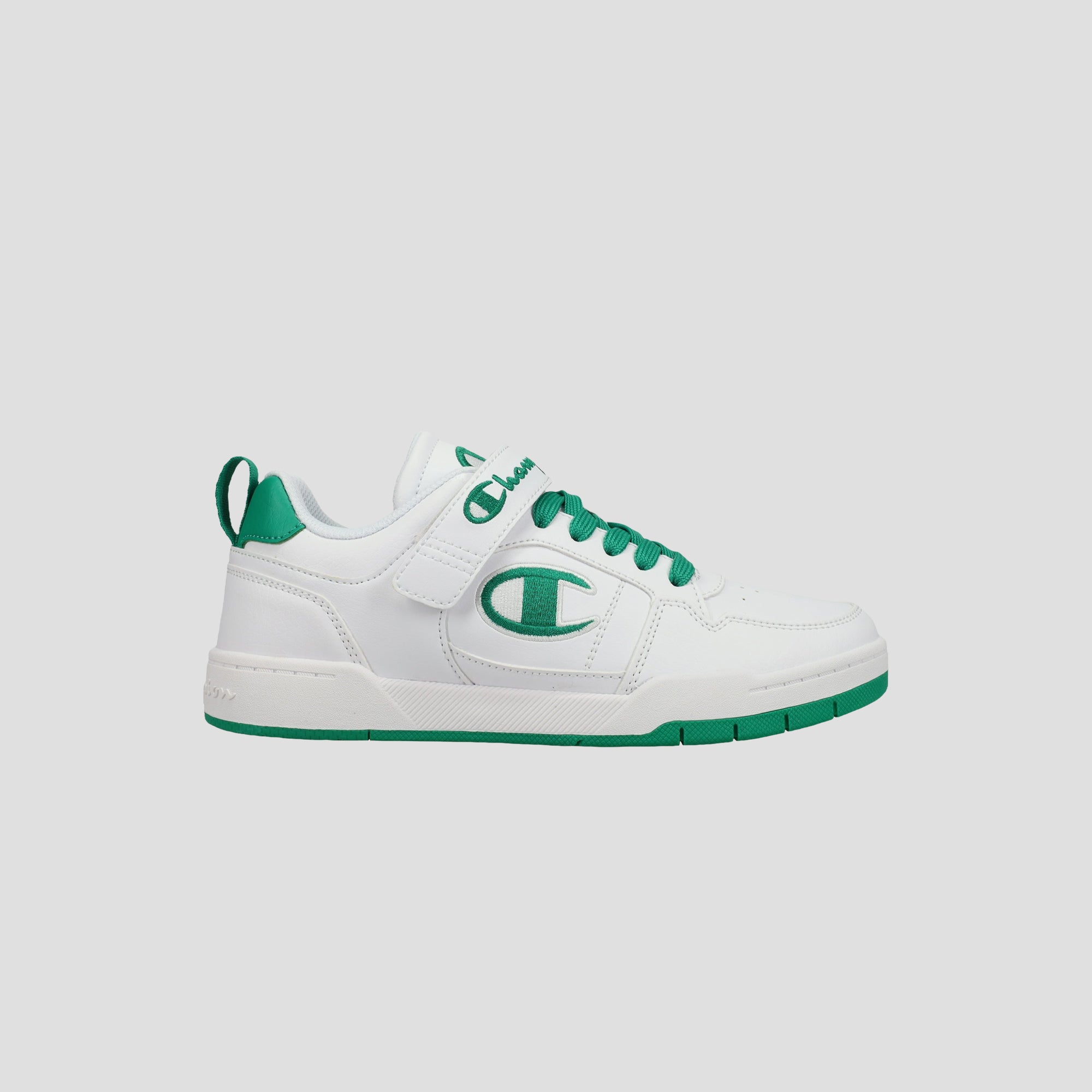 The Champion Kids' Arena Power Low sneaker features a white design with green accents, green laces, a green side logo, plus a green sole and heel tab. Shown on a light gray background, it delivers classic Champion style for kids.