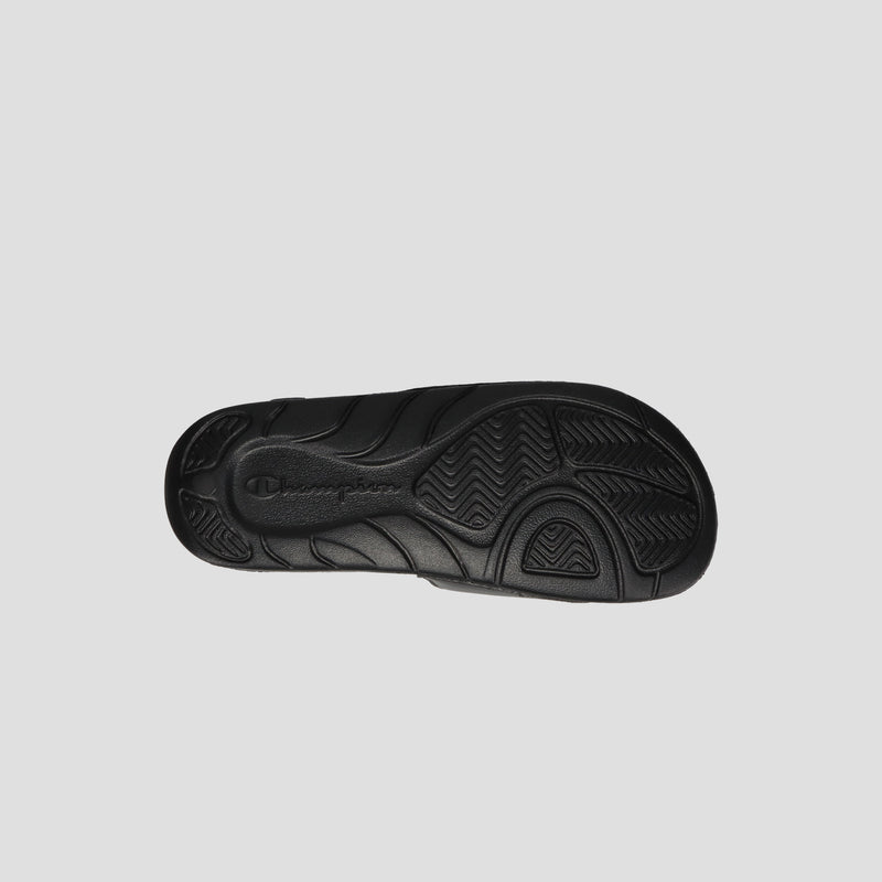 The Champion Kids' Mega SFB Slide features a black rubber sole with a wavy textured tread and an embossed logo near the heel, offering lightweight comfort and a contoured footbed, shown on a plain light gray background.