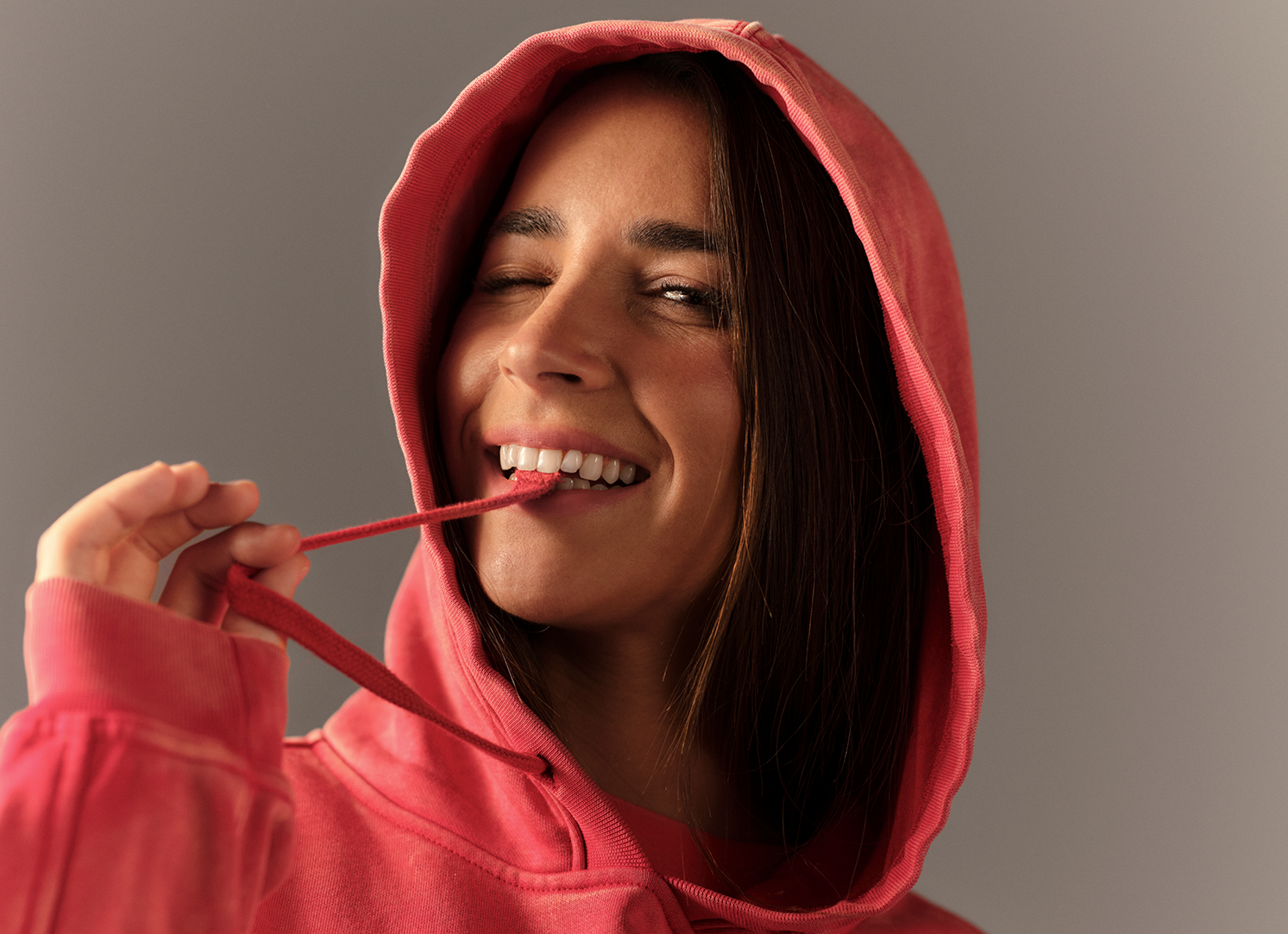 Person wearing a red hoodie biting it's drawstring against a gray background