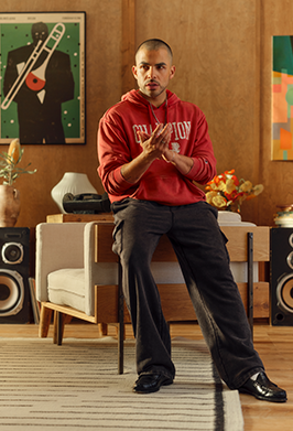 Man in a red hoodie sitting in a stylish room with decor and furniture.