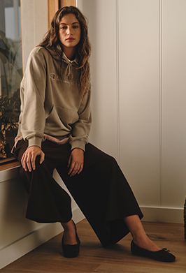 Woman sitting on a windowsill wearing a beige sweater and black pants.