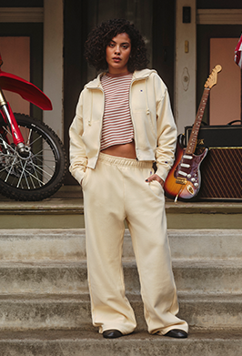 Woman in beige outfit standing on steps with a motorcycle and guitar in the background