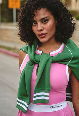 Woman wearing a pink dress with green accents and a green scarf outdoors.