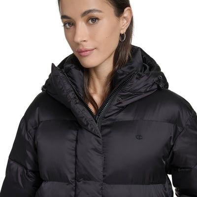 A woman with straight brown hair wears the Champion Maxi Length Cinch Waist Hooded Puffer. She stands against a plain white background with a neutral expression, facing slightly to the side.