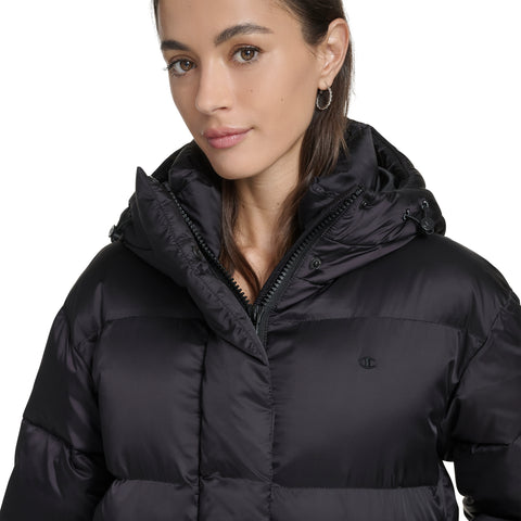 A woman with straight brown hair wears the Champion Maxi Length Cinch Waist Hooded Puffer. She stands against a plain white background with a neutral expression, facing slightly to the side.