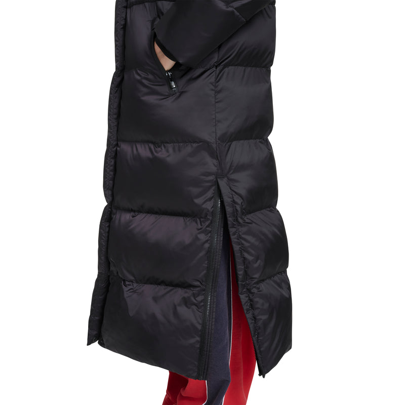 A close-up of a person wearing the Champion Maxi Length Cinch Waist Hooded Puffer with a side zipper slightly open, revealing red and navy pants underneath.