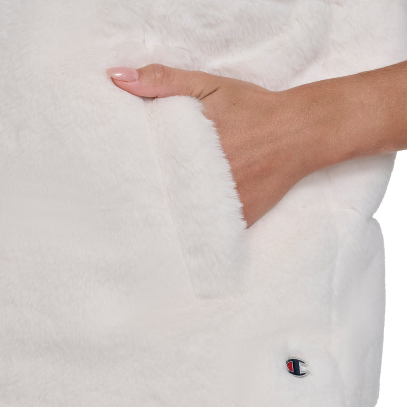 A hand with light pink nail polish is partially tucked into the pocket of a soft, white Champion Puffer Vest. A small, embroidered Champion logo near the pocket adds iconic flair to this cozy outerwear style.