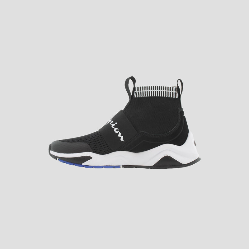The Champion Kids' Rally Pro is a black and white sock-style ankle shoe with a thick sole, high ankle collar, pull tabs, and white cursive branding. The light gray sole features blue accents.