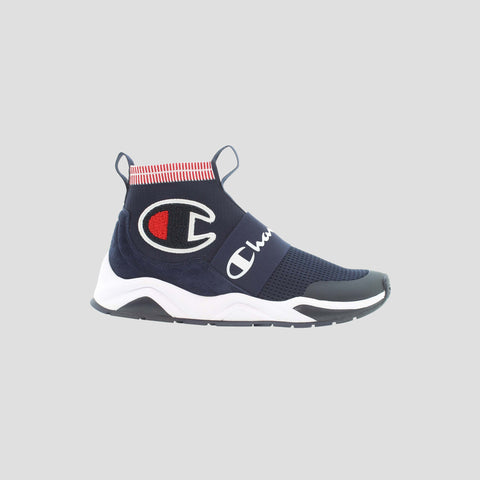 The Men's Rally Pro by Champion is a navy blue slip-on athletic shoe with a cushioned insole, white sole, red and white striped ankle collar, a large “C” logo, and “Champion” text across the midfoot strap.