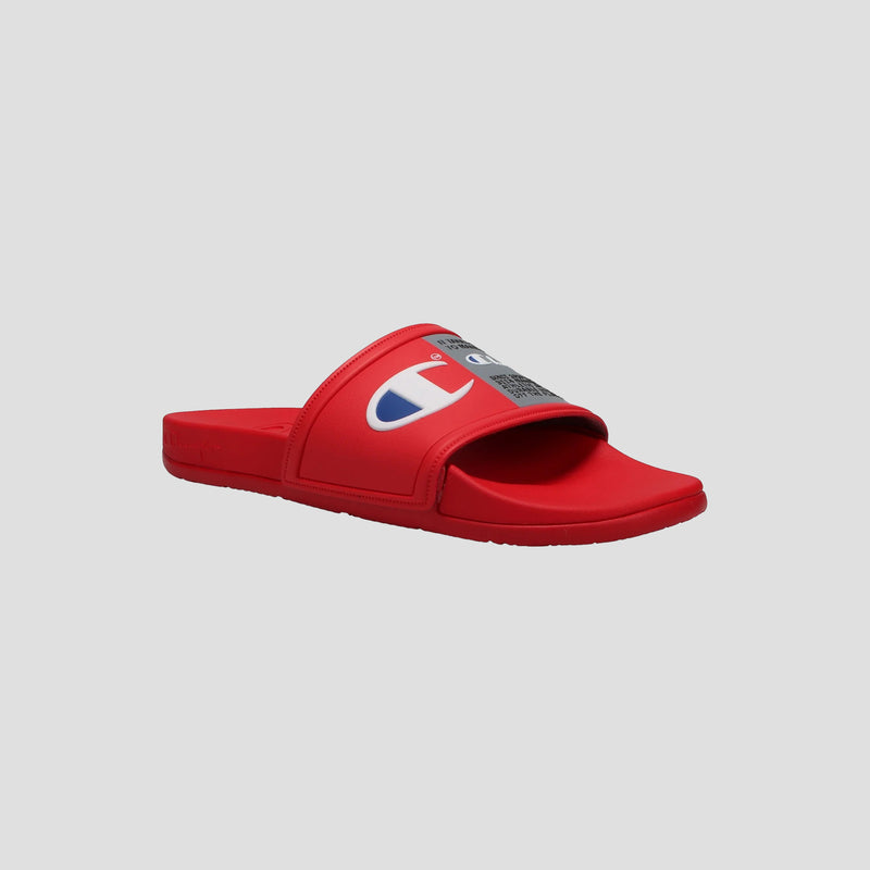 The Champion Men's IPO Squish Slide in red features a contoured footbed, wide strap with blue and white Champion logo, and is shown on a gray background. These lightweight slides combine comfort with style.