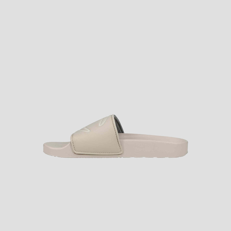 The Champion Women's IPO Slide is a beige sandal with a wide strap and open toe, offering lightweight comfort and a contoured footbed, shown on a plain light gray background.