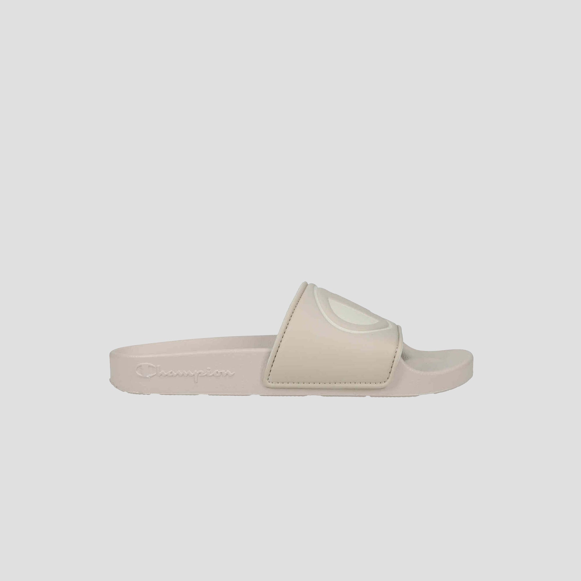 The Champion Women's IPO Slide is a beige sandal with a wide, raised-logo strap, lightweight comfort, contoured footbed, and textured sole, shown on a plain light gray background.