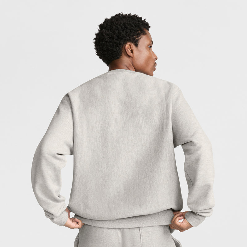 A person with short curly hair is wearing a Champion Reverse Weave Crewneck Sweatshirt and matching pants, standing with their back to the camera against a plain white background.