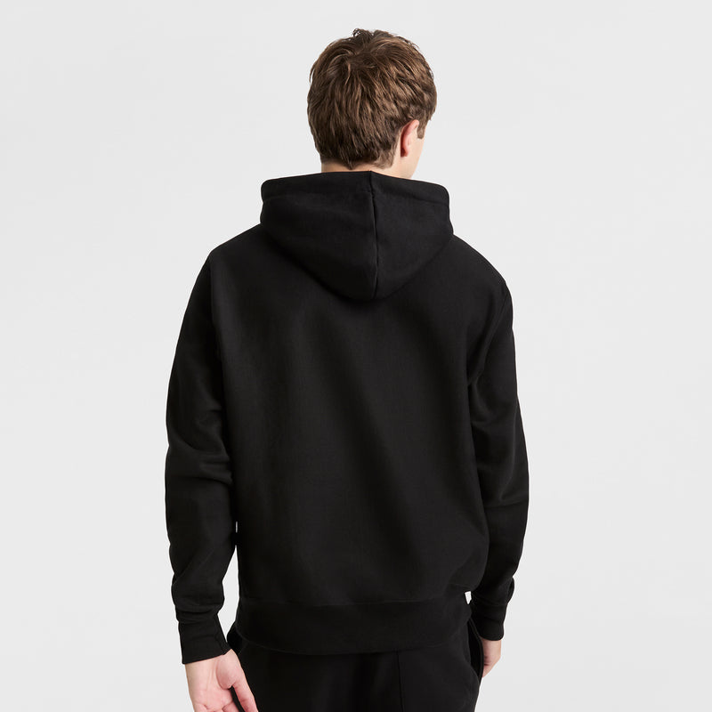 A person with short brown hair, seen from behind, wears a plain black Champion Reverse Weave Hoodie and black pants against a plain white background.