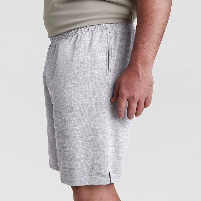 A person in light gray Champion 10" Moisture Wicking Sport Shorts - Big & Tall and a beige shirt is shown from the side with their right arm relaxed, against a plain light background.