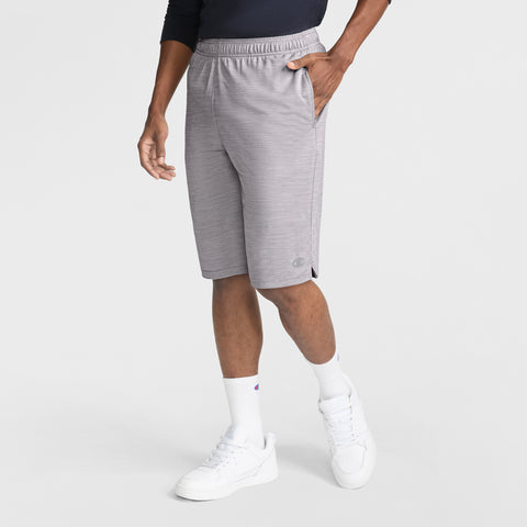 A person wearing Champion 10" Moisture Wicking Sport Shorts in light gray, a dark long-sleeve shirt, white crew socks, and white sneakers stands with one hand in their pocket against a plain white background.