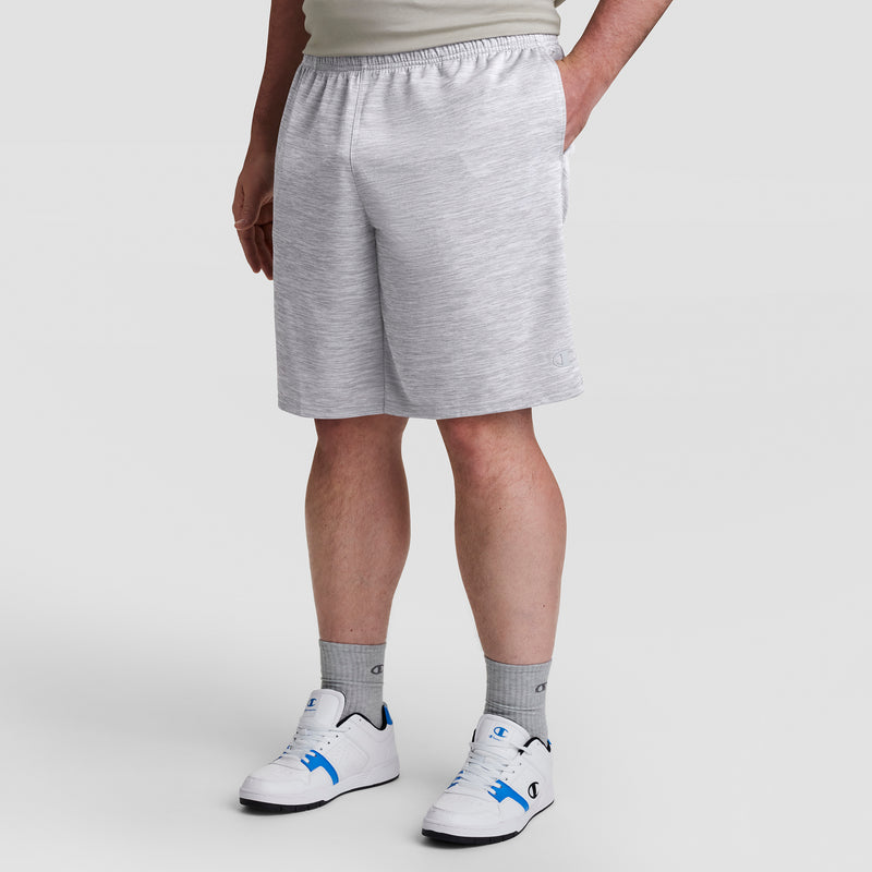A person models Champion's 10" Moisture Wicking, Sport Shorts - Big & Tall in light gray, paired with gray socks and white sneakers with blue accents against a plain background. Only the lower half of their body is shown.